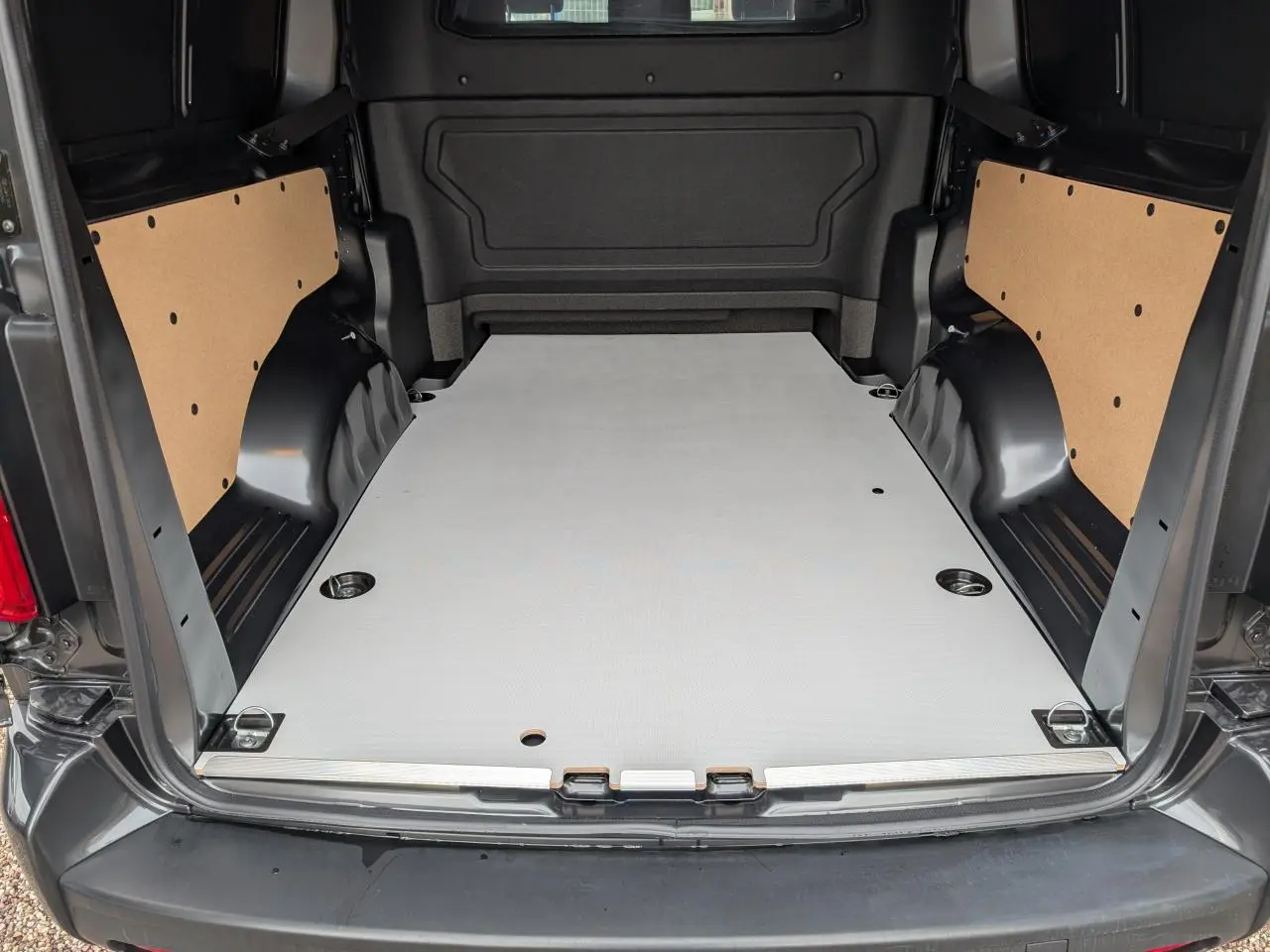 Vue arrière du Citroën Jumpy gris 2025, plancher bois clair et panneaux latéraux en bois brut visibles dans l'espace de chargement.
