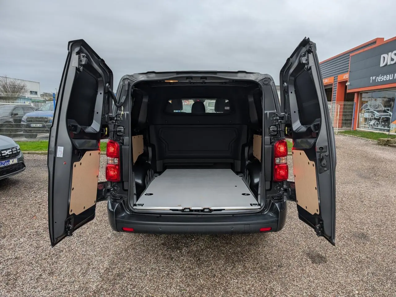 Vue arrière d'un Citroën Jumpy gris 2025 avec portes battantes ouvertes et plancher bois visible dans la zone de chargement.