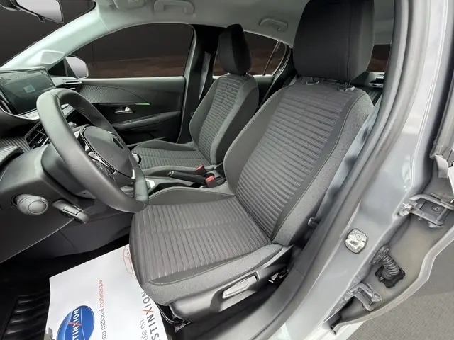 Vue intérieure côté conducteur de la Peugeot 208 100CH S&S Active 2024 gris foncé, sièges tissu et volant cuir multifonctions.