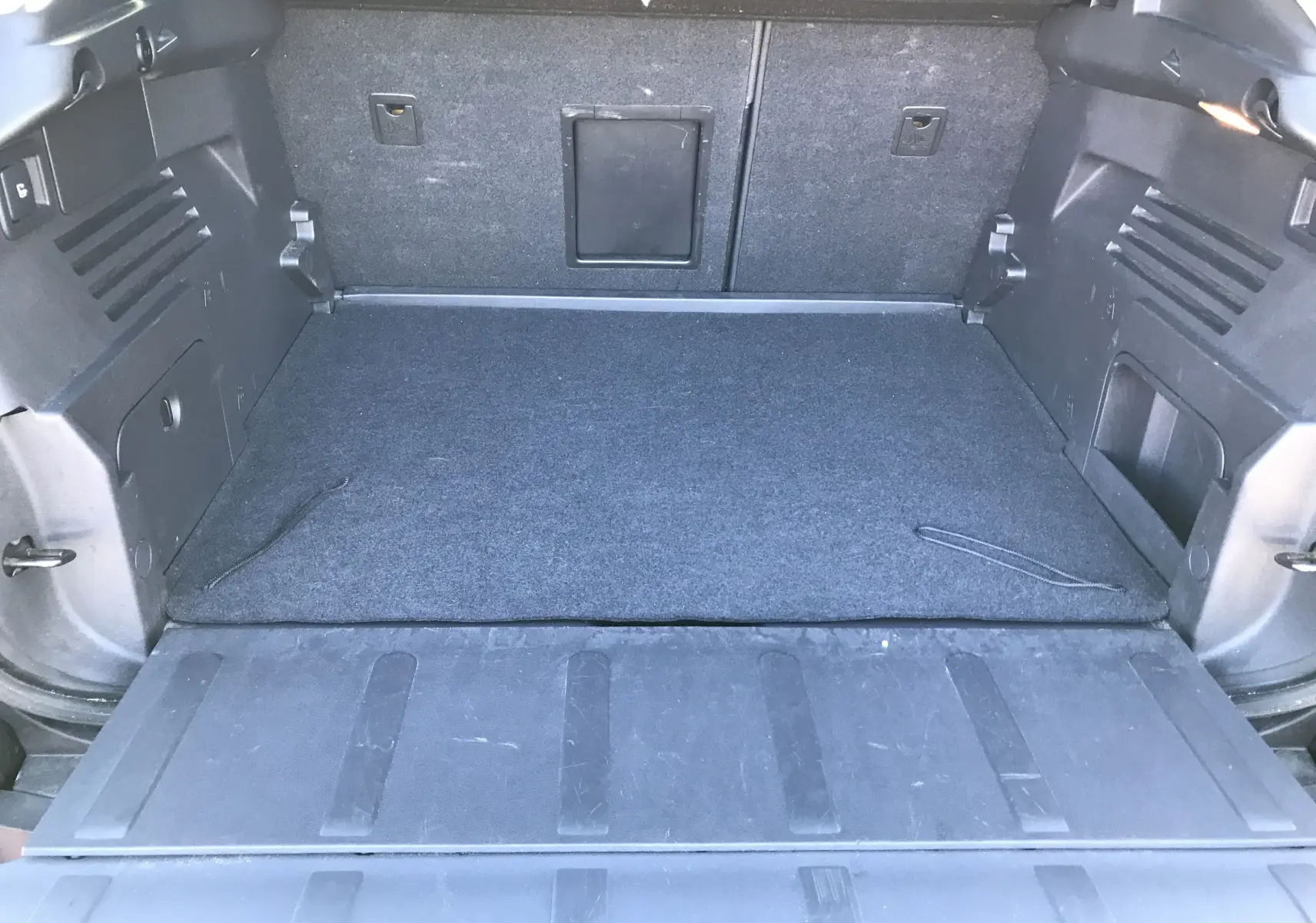 Coffre ouvert vu de l'arrière d'un Peugeot 3008 Business bleu Bourrasque avec tapis de sol gris et rangements latéraux.