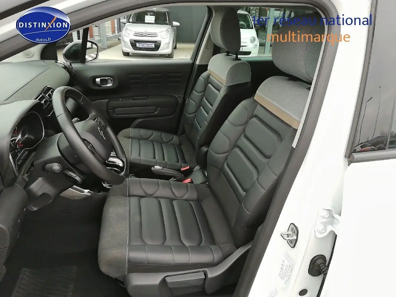 Vue intérieure côté conducteur d'une Citroën C3 Aircross blanc polar, sièges en cuir noir et tissu gris clair.