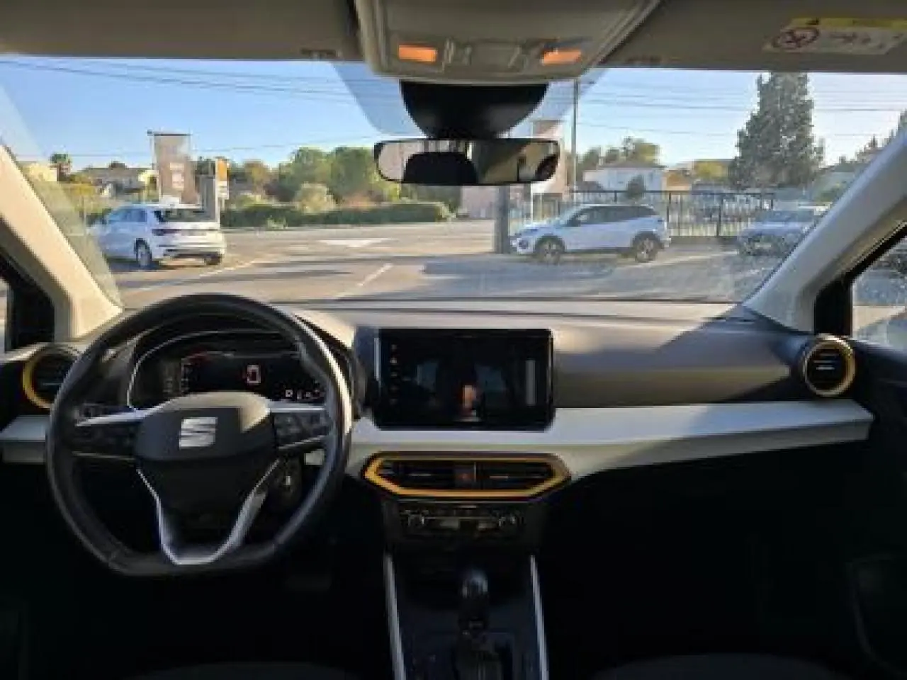 Vue intérieure avant du SEAT Arona 2024 avec tableau de bord clair, volant cuir multifonction et écran tactile central.