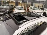 Vue en plongée sur le toit ouvrant panoramique d’un KIA Xceed blanc 2021 hybride rechargeable, entouré de plusieurs véhicules.