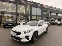 KIA Xceed 1.6 GDI blanc hybride rechargeable, vue 3/4 avant droite devant un concessionnaire en 2021.