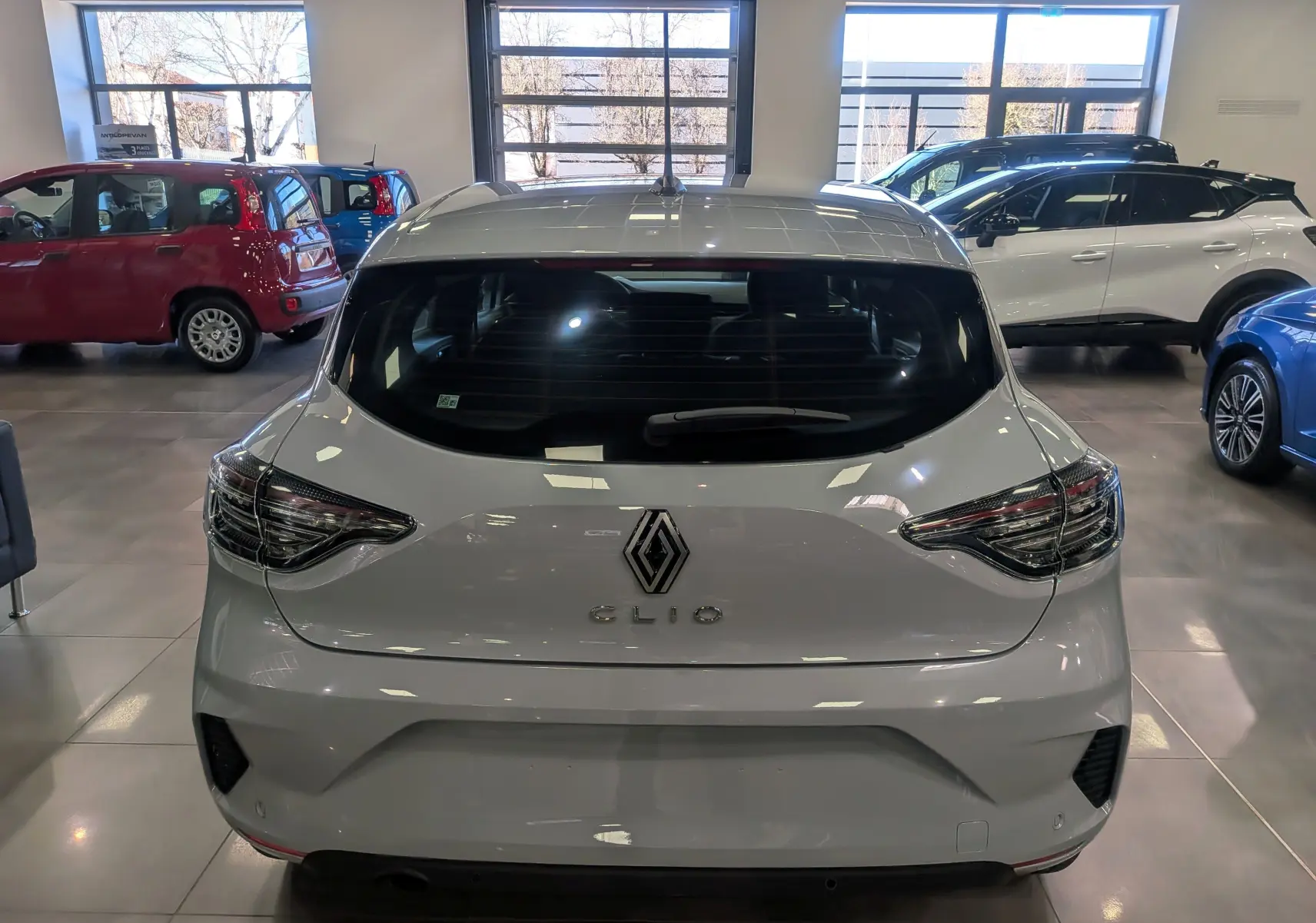 Vue arrière d'une Renault Clio V gris Rafale 2025 avec feux LED et caméra de recul visible en intérieur showroom.