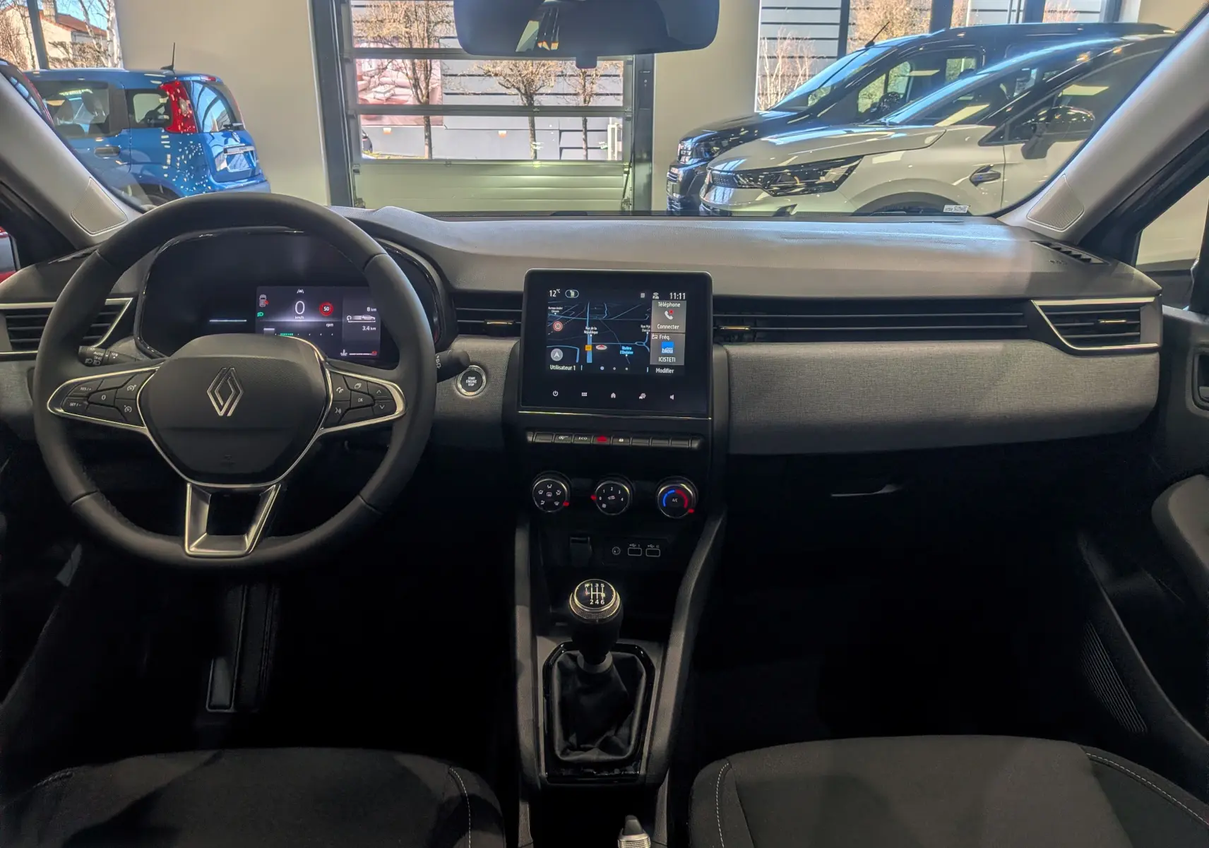 Vue intérieure avant de la Renault Clio V gris Rafale, avec tableau de bord moderne et boîte manuelle visible.