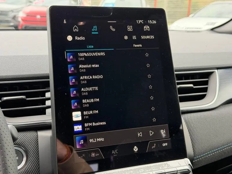 Vue rapprochée de l’écran tactile central du Renault Captur 2026, affichant les stations radio avec intérieur noir et surpiqûres bleues.