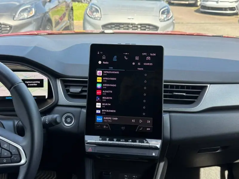 Vue intérieure du tableau de bord du Renault Captur rouge 2025 avec écran tactile central vertical et volant multifonction.
