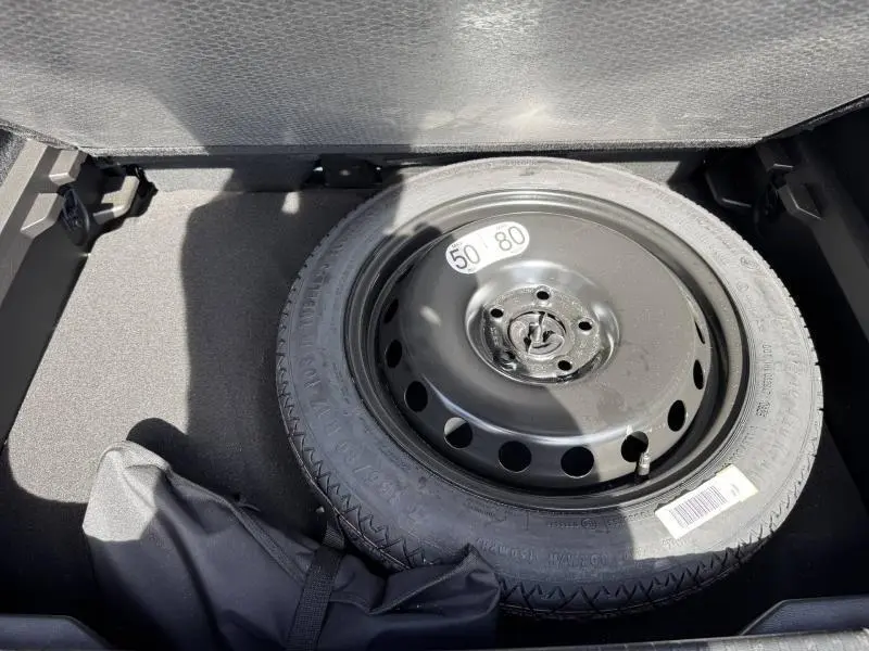 Vue rapprochée de la roue de secours noire dans le coffre d’un Renault Captur rouge 2025, version hybride.