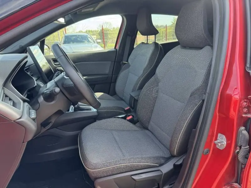 Vue intérieure côté conducteur du Renault Captur rouge 2025, sièges tissu gris et volant multifonction visible.