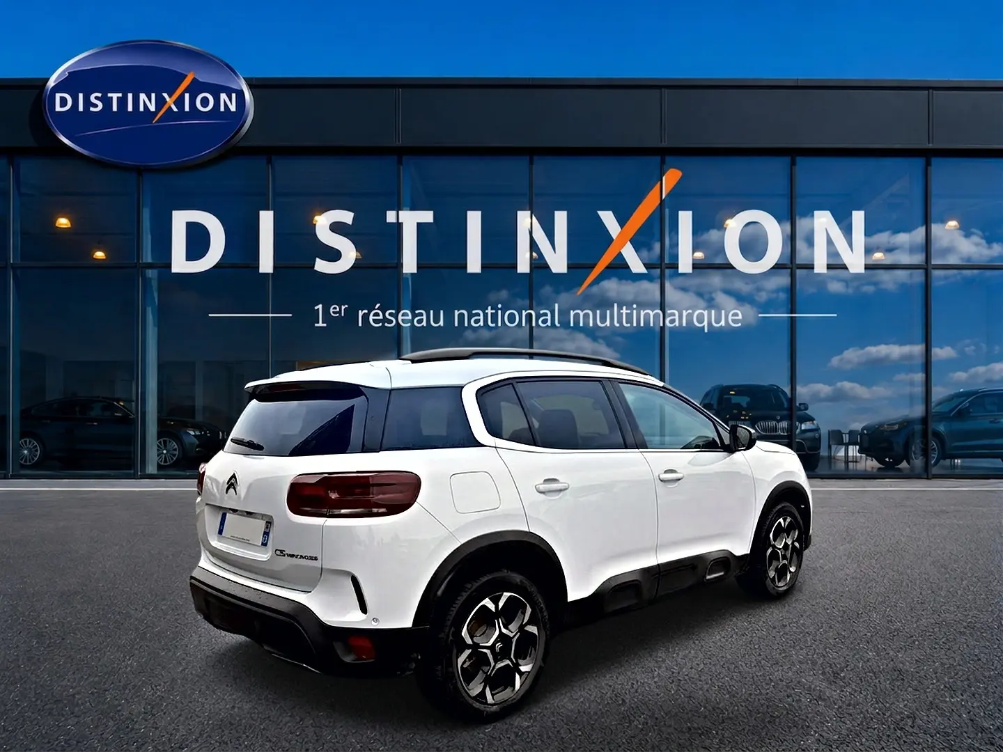 Vue 3/4 arrière droite d'un Citroën C5 Aircross blanc avec jantes alu et vitres arrière teintées, devant un bâtiment vitré.