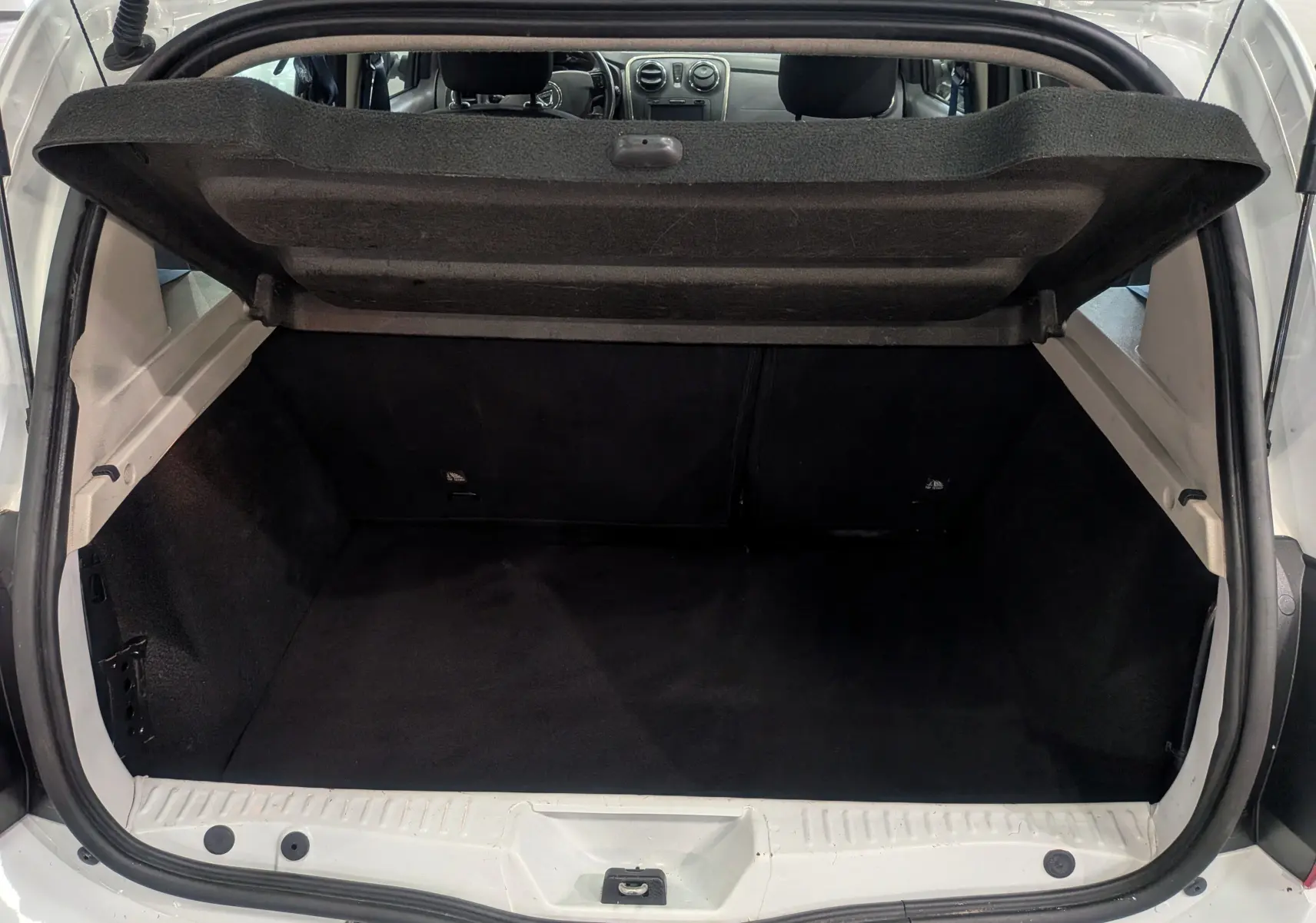 Coffre ouvert vu de l'arrière d'une Dacia Sandero blanc glacier, montrant l'espace de chargement vide et l'intérieur noir.