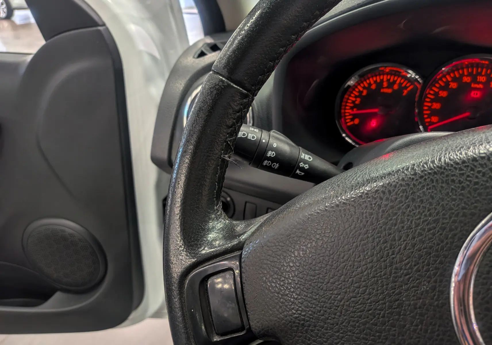 Gros plan sur le volant noir et le tableau de bord éclairé en rouge d'une Dacia Sandero Blanc Glacier, côté conducteur.