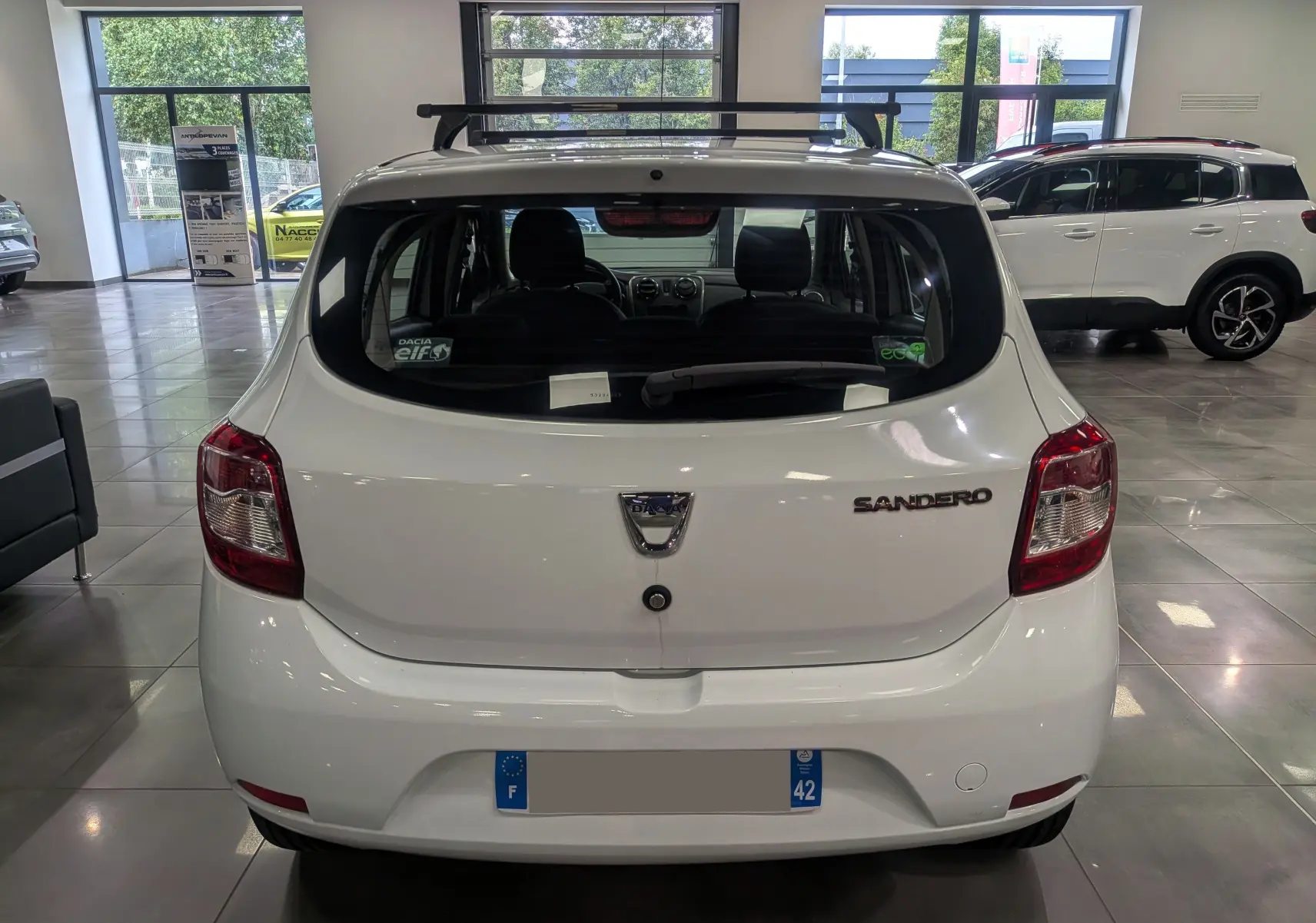 Vue arrière d'une Dacia Sandero blanc glacier en showroom, avec logo et badge modèle bien visibles.