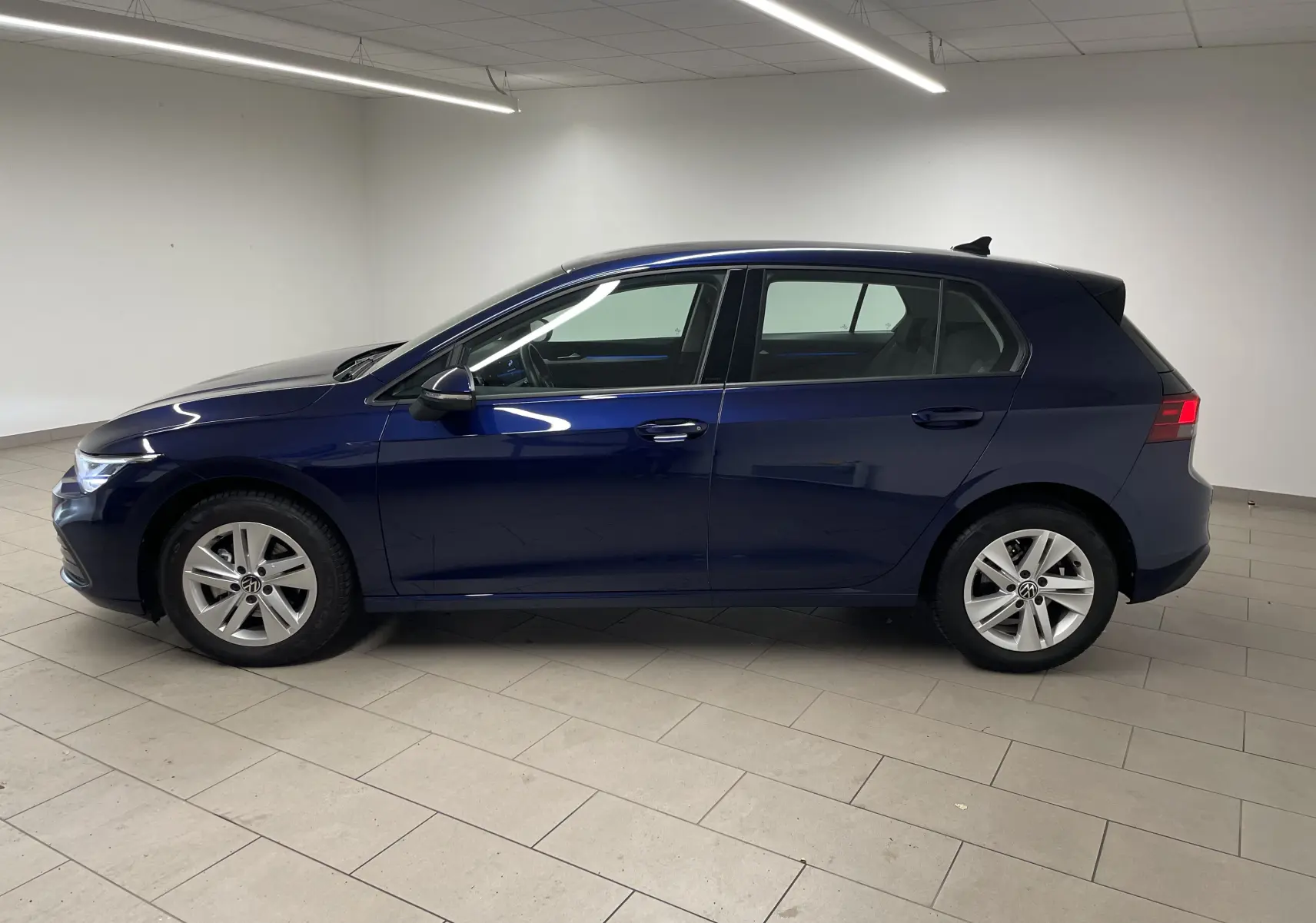 Profil côté gauche d'une Volkswagen Golf 1.0 TSI 110 DSG7 Life Plus 2023 en bleu Atlantique métallisé, en intérieur.