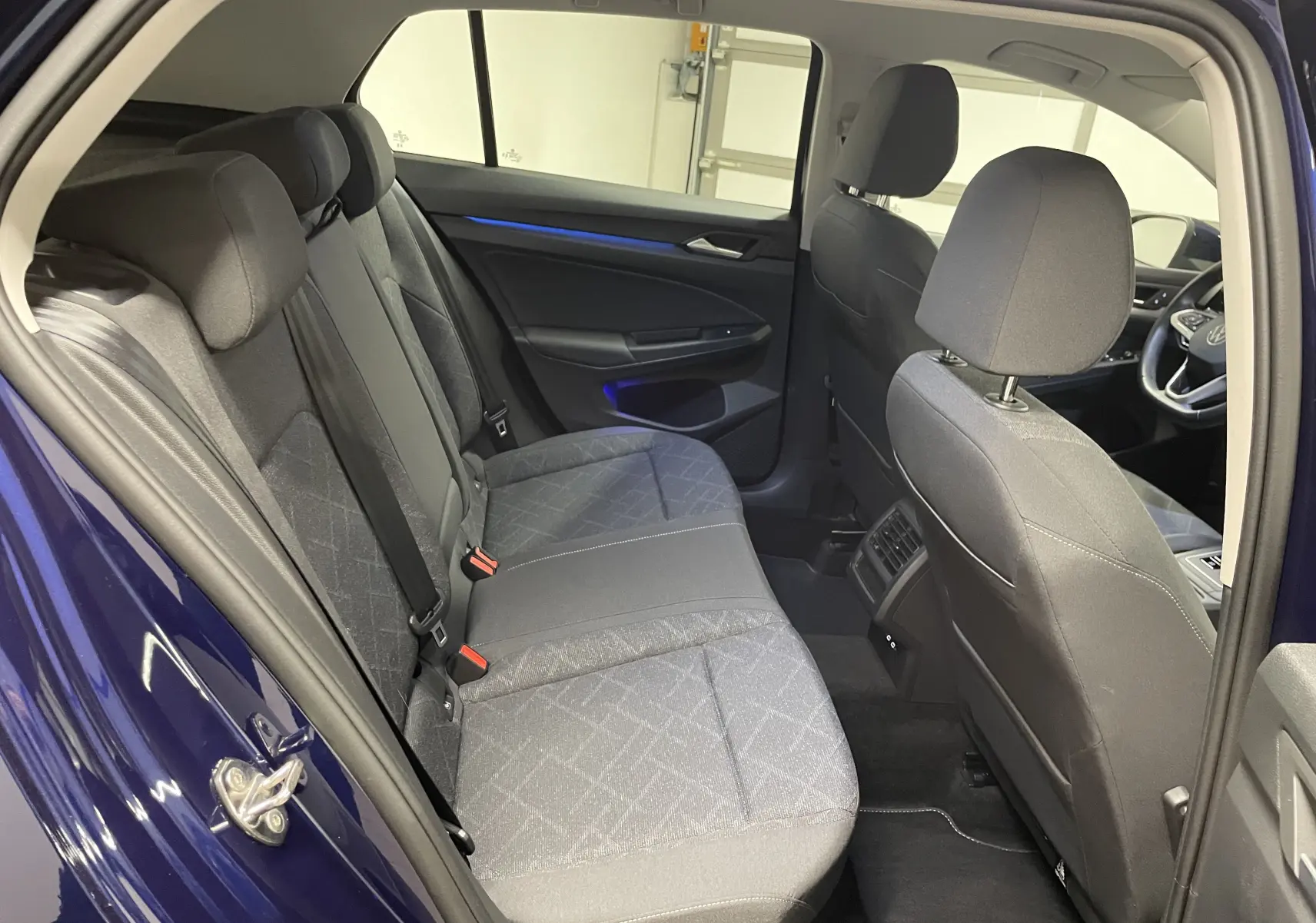 Vue intérieure arrière côté gauche d'une Volkswagen Golf 2023 bleu Atlantique, montrant les sièges arrière et l'habitacle avant.
