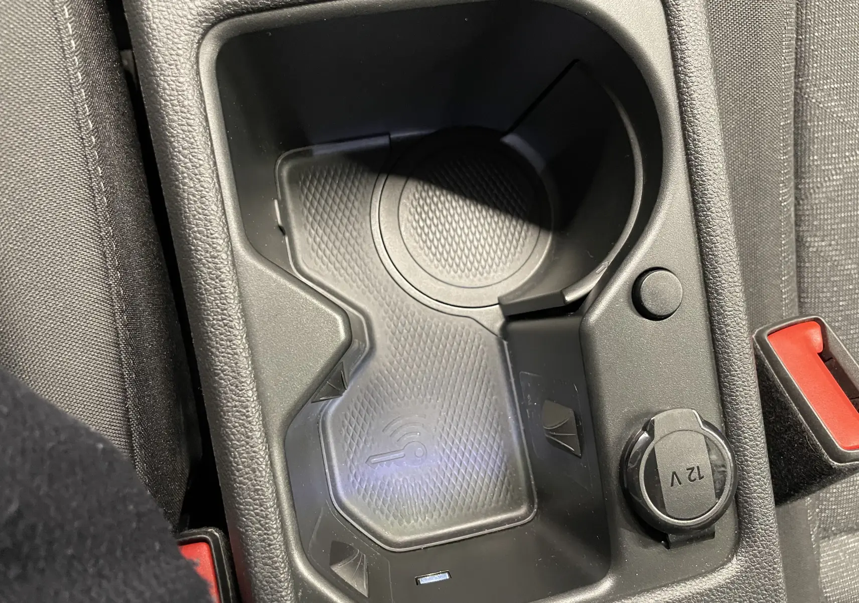 Gros plan sur le compartiment central avec chargeur sans fil et prise 12V dans l'habitacle noir d'une Volkswagen Golf.