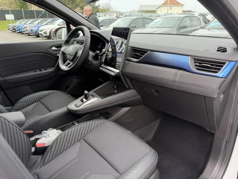 Intérieur avant droit du Renault Captur 2026 hybride, avec tableau de bord noir et insert bleu nacré, écran tactile vertical.
