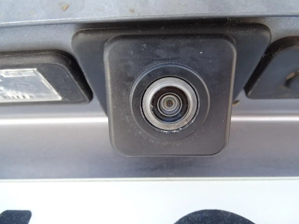 Gros plan sur la caméra de recul noire intégrée au hayon d’un Peugeot 3008 gris Artense, vue arrière.
