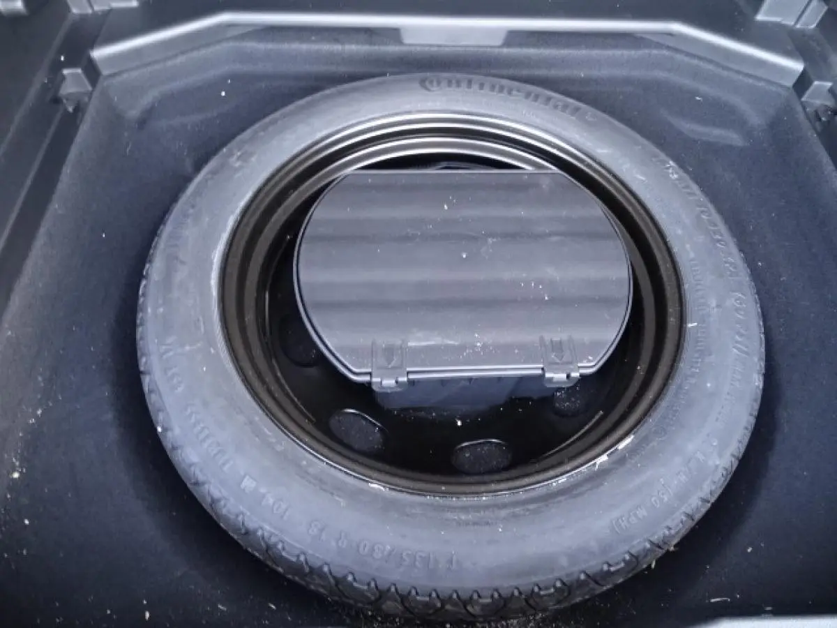 Gros plan sur la roue de secours galette noire dans le coffre du Peugeot 3008 gris Artense, vue de dessus.