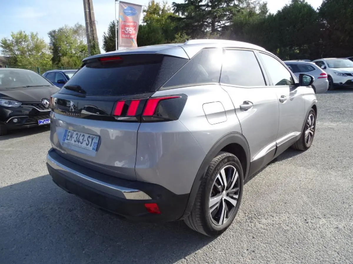 Vue 3/4 arrière droite d’un Peugeot 3008 gris Artense avec barres de toit en aluminium et feux arrière à griffes rouges.