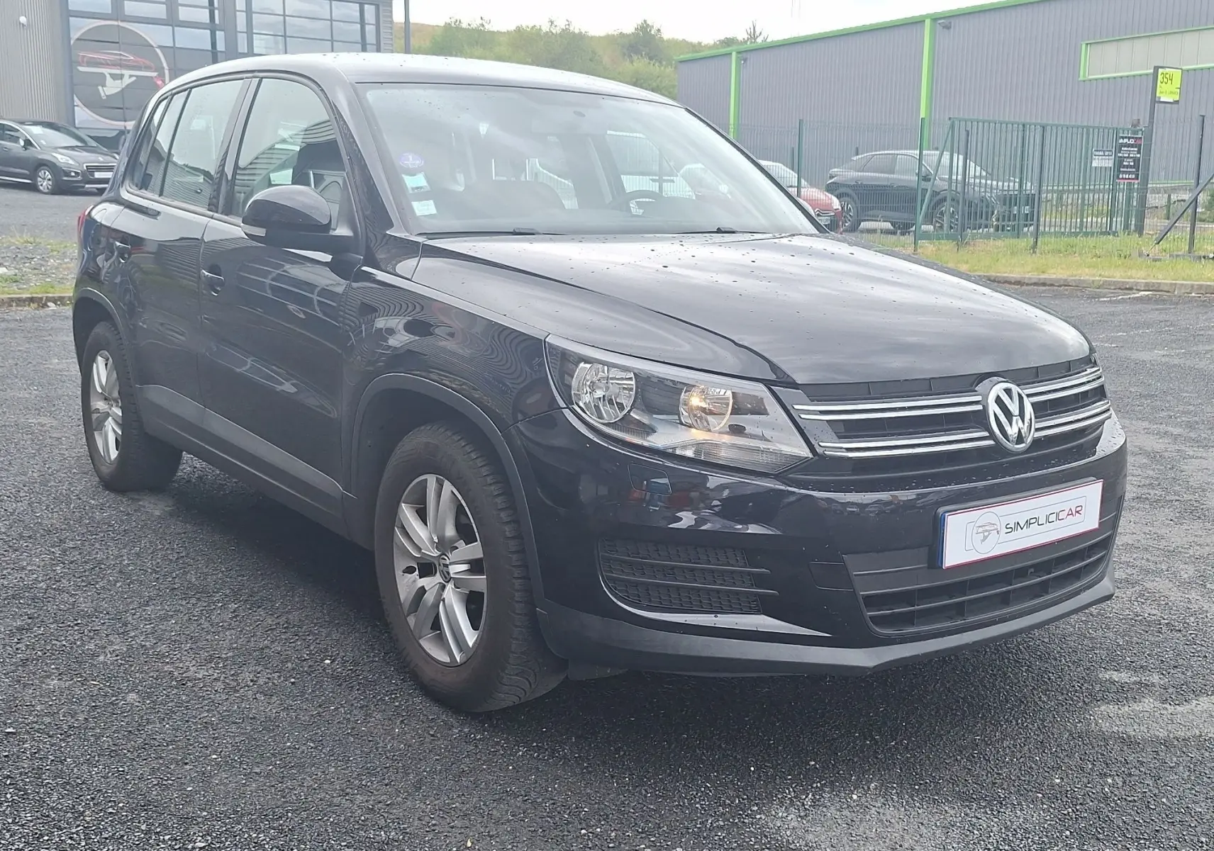 Volkswagen Tiguan noir 2014 en 3/4 avant droit, avec jantes alliage 16 pouces et phares allumés.