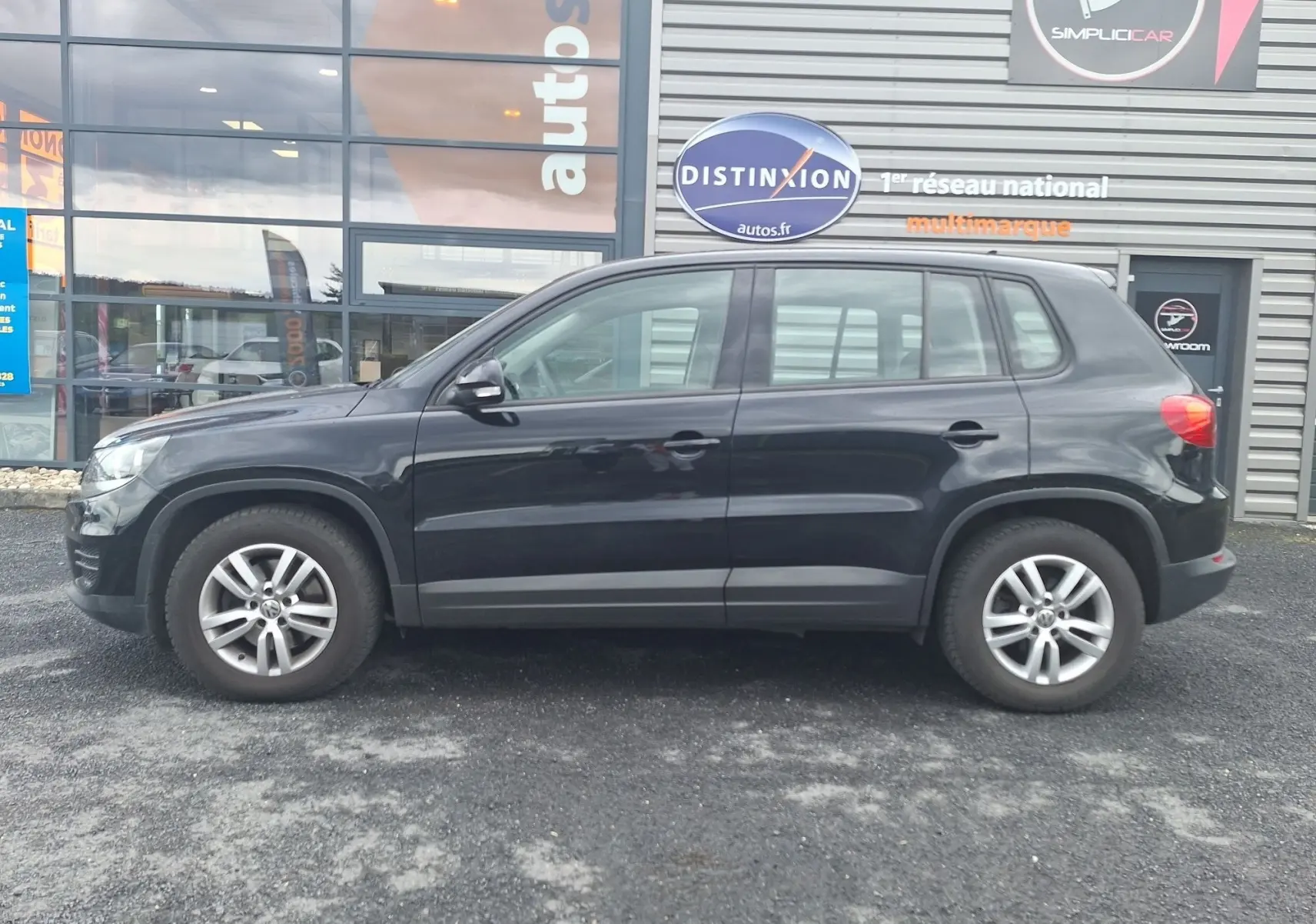 Profil côté gauche d'un Volkswagen Tiguan noir 2014 avec jantes alliage 16 pouces, garé devant un bâtiment commercial.