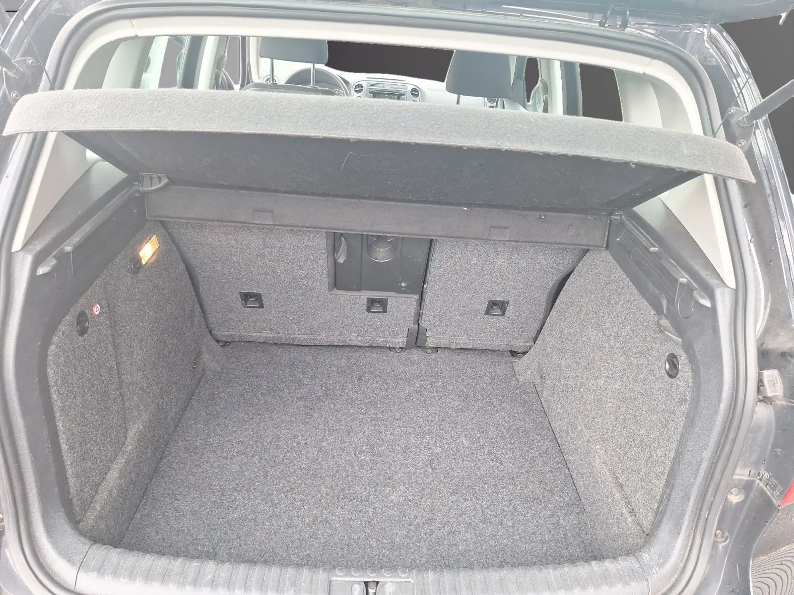 Coffre ouvert d’un Volkswagen Tiguan noir 2014, vue arrière montrant l’espace de chargement et la tablette cache-bagages relevée.