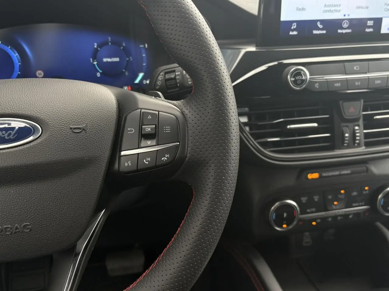 Gros plan sur le volant perforé noir à surpiqûres rouges et le tableau de bord numérique du Ford Kuga 2023.