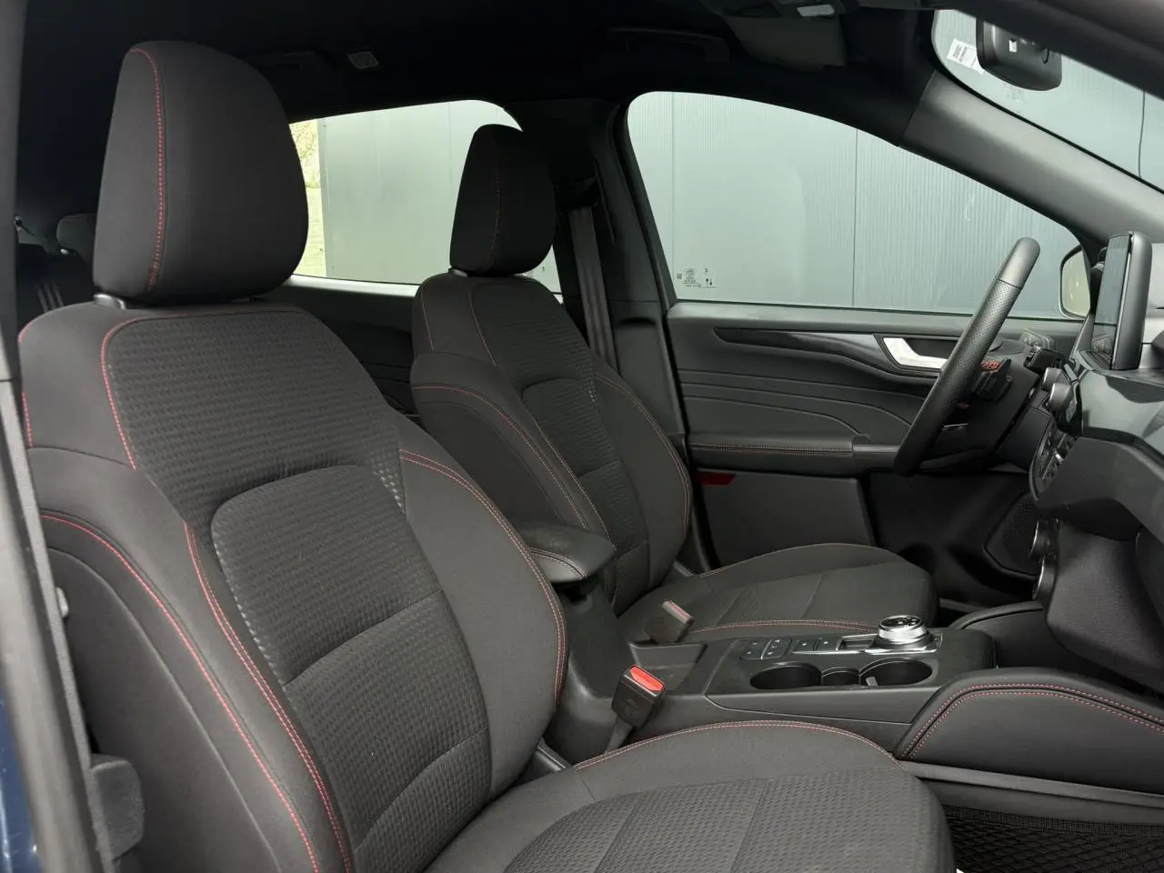 Vue intérieure côté droit du Ford Kuga 2023, sièges noirs avec surpiqûres rouges et console centrale avec sélecteur rotatif.