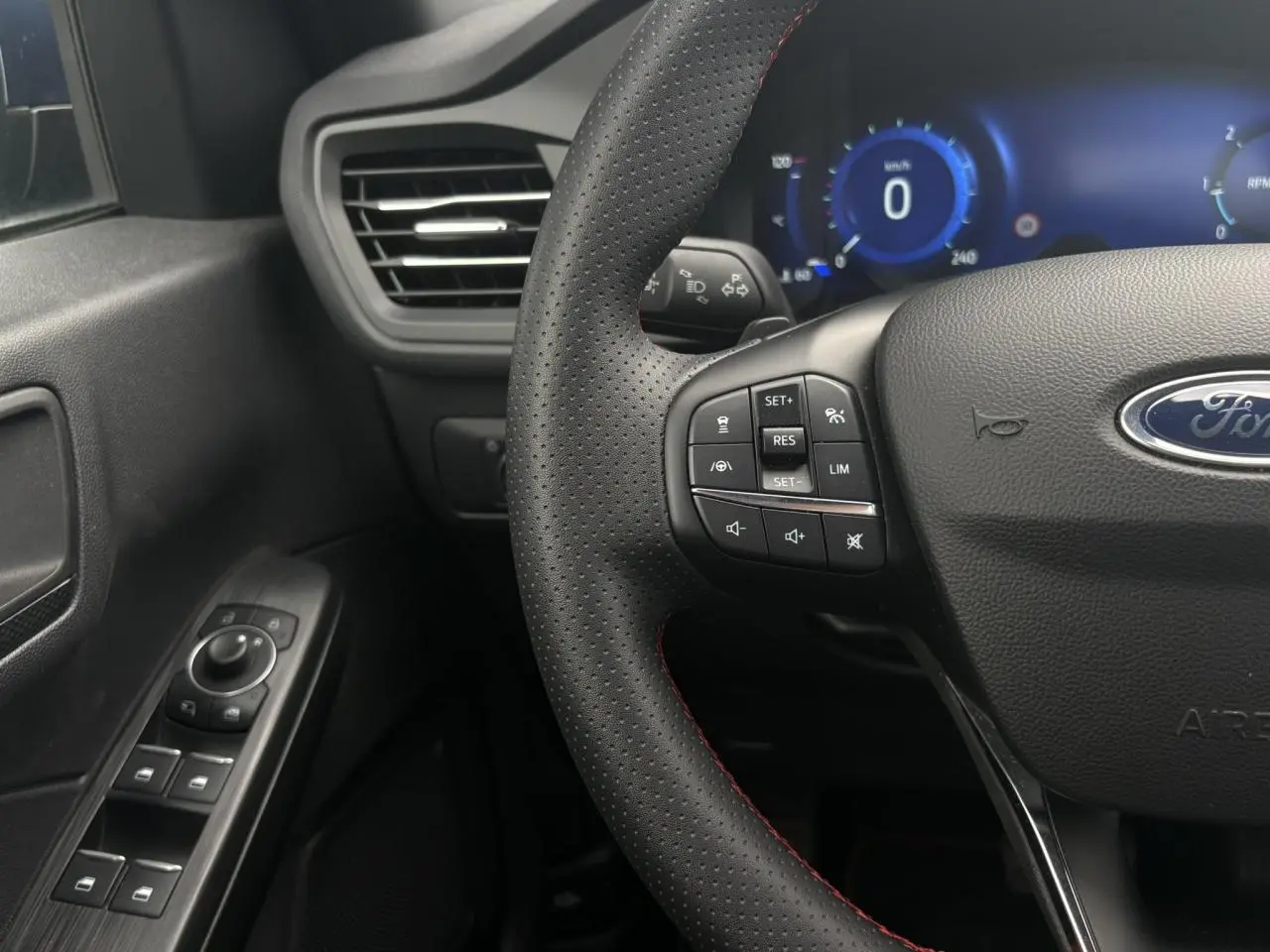 Gros plan sur le volant perforé noir avec surpiqûres rouges et tableau de bord numérique bleu du Ford Kuga 2023.