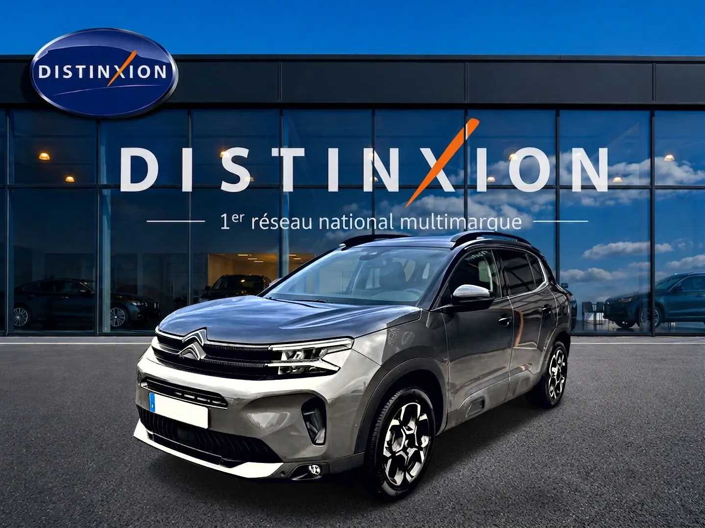 Citroën C5 Aircross gris platinium en 3/4 avant droit, avec jantes alu et barres de toit visibles devant showroom Distinxion.