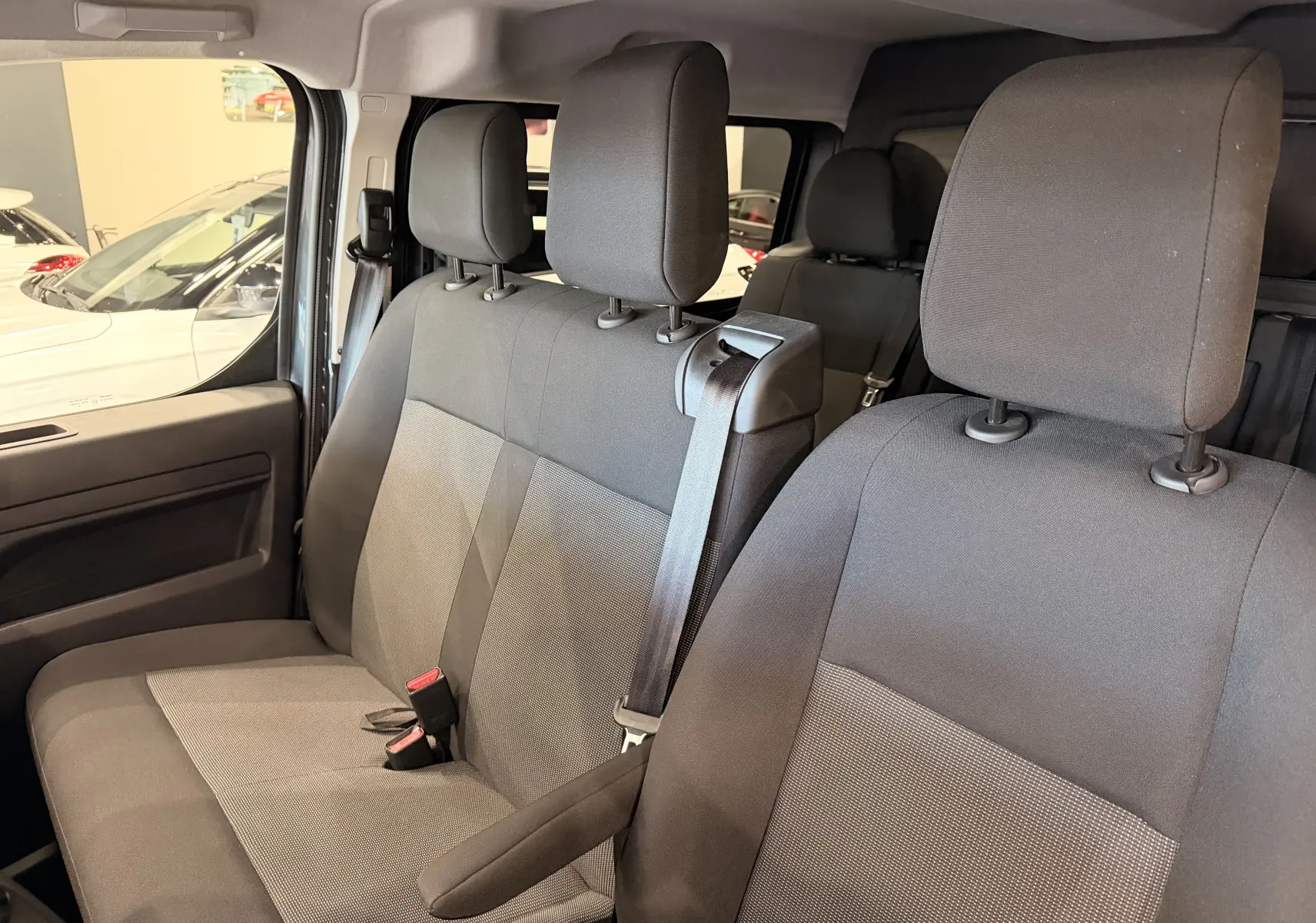 Vue intérieure côté conducteur du Citroën Jumpy cabine approfondie 2025, sièges tissu gris avec ceinture et appuie-tête visibles.