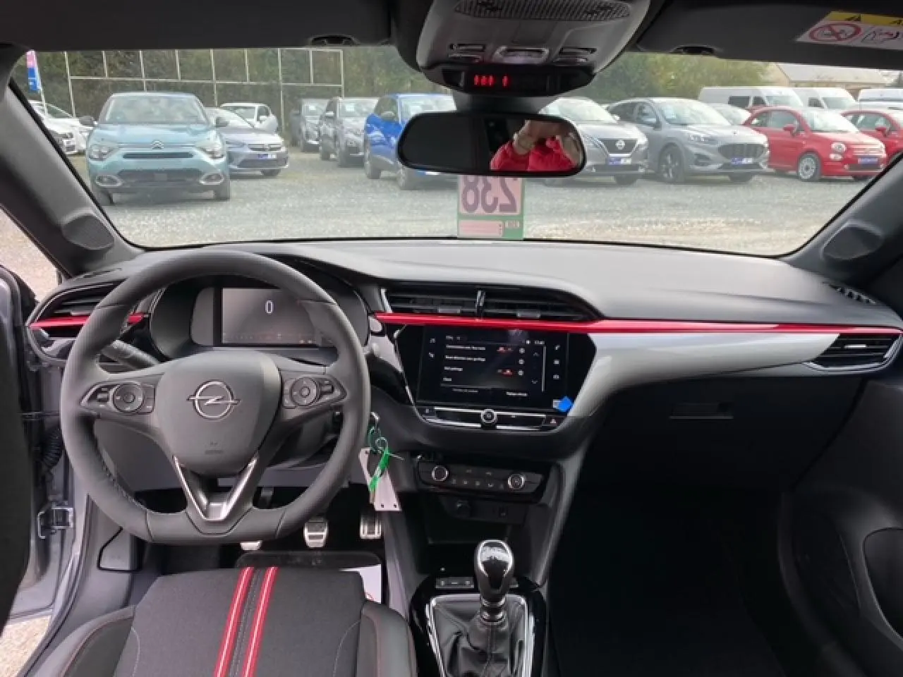 Intérieur avant de l’Opel Corsa gris Magnetic 2022, volant multifonction, tableau de bord noir avec bande rouge et écran tactile central.
