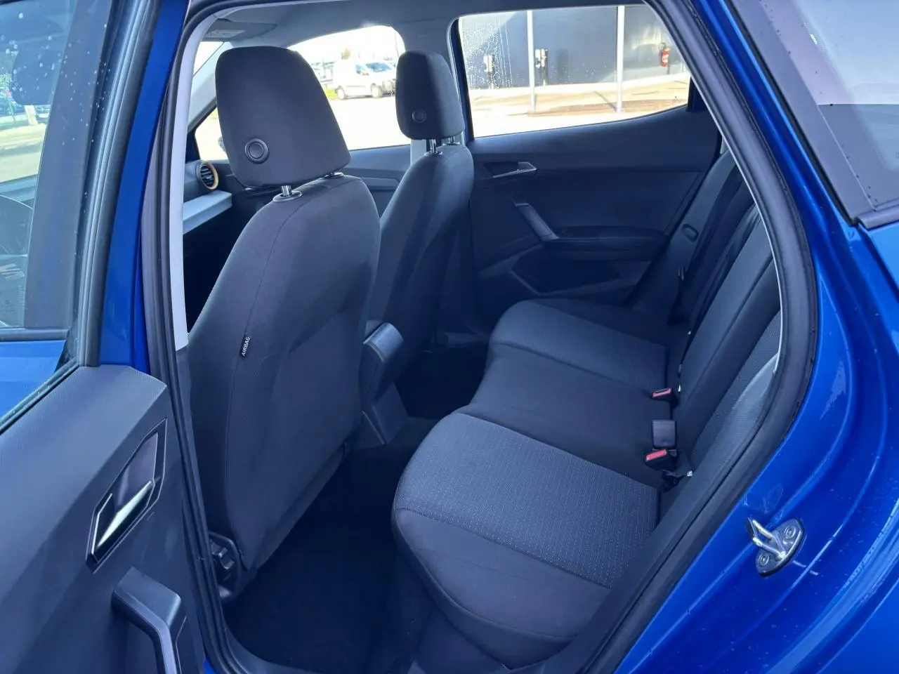 Vue côté droit de l'habitacle arrière du SEAT Arona bleu saphir, montrant les sièges en tissu noir et la porte ouverte.