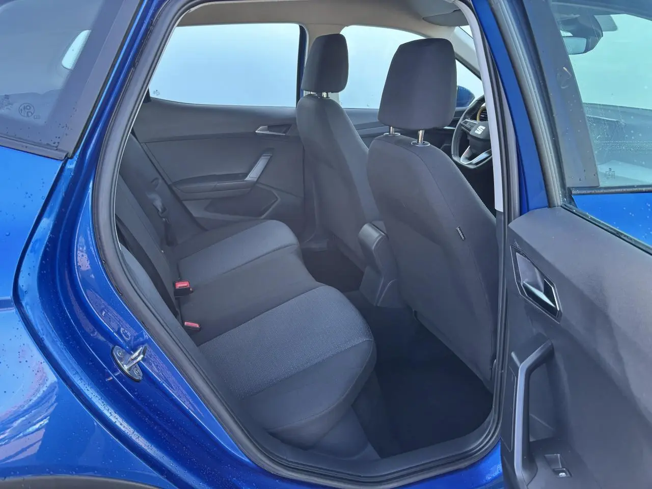 Vue intérieure côté arrière gauche d'une SEAT Arona bleu saphir avec sièges tissu noirs et portière ouverte.
