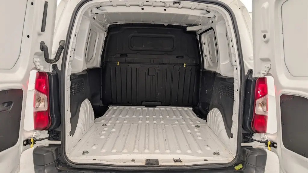 Vue arrière du Citroën Berlingo Fourgon blanc Banquise montrant l'espace de chargement vide avec cloison noire et feux arrière allumés.