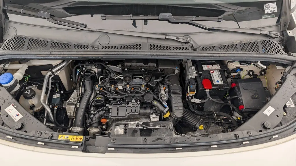Vue plongeante sur le moteur diesel du Citroën Berlingo Van blanc banquise, montrant les composants sous le capot ouvert.