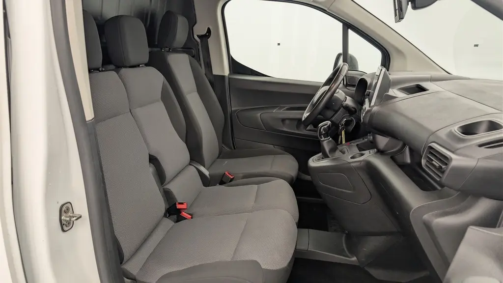 Vue intérieure côté conducteur du Citroën Berlingo Van blanc, montrant les sièges tissu gris et le tableau de bord avec écran tactile.