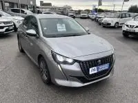 Peugeot 208 1.2 PureTech 100 Style gris vue 3/4 avant droit sur parking avec calandre noire et phares LED distinctifs.