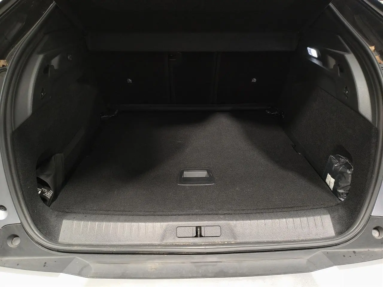 Coffre ouvert vu de l'arrière d'un Peugeot 3008 Hybrid gris Artense, espace de chargement vide et éclairé.