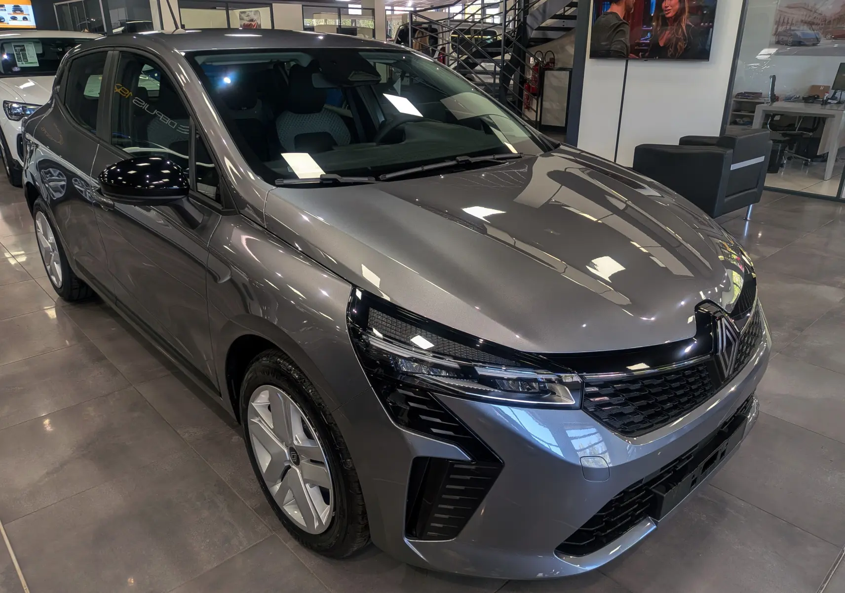 Renault Clio V Blue dCi 100 gris schiste en 3/4 avant droit, avec calandre noire et jantes spécifiques en concession.