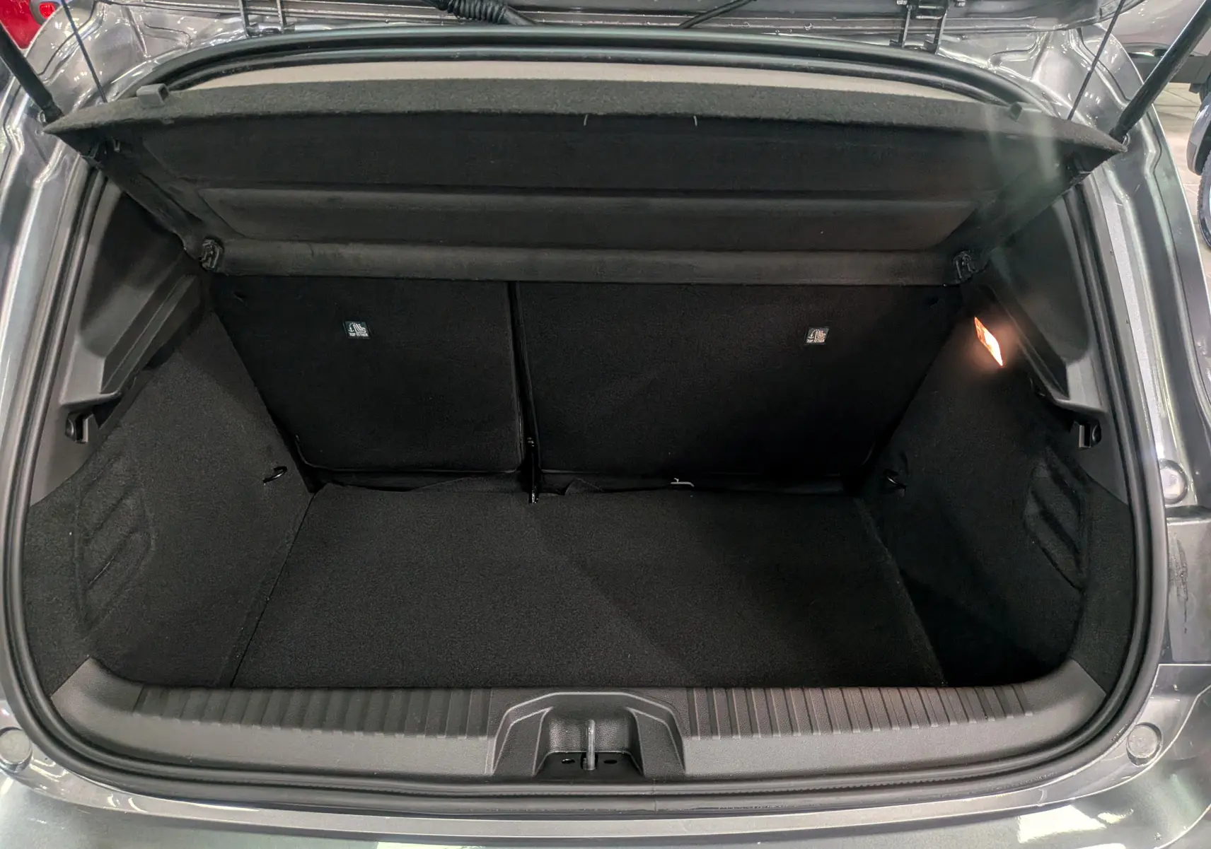 Coffre ouvert de Renault Clio V gris schiste, vue arrière montrant l'espace de chargement et l'éclairage intérieur à droite.