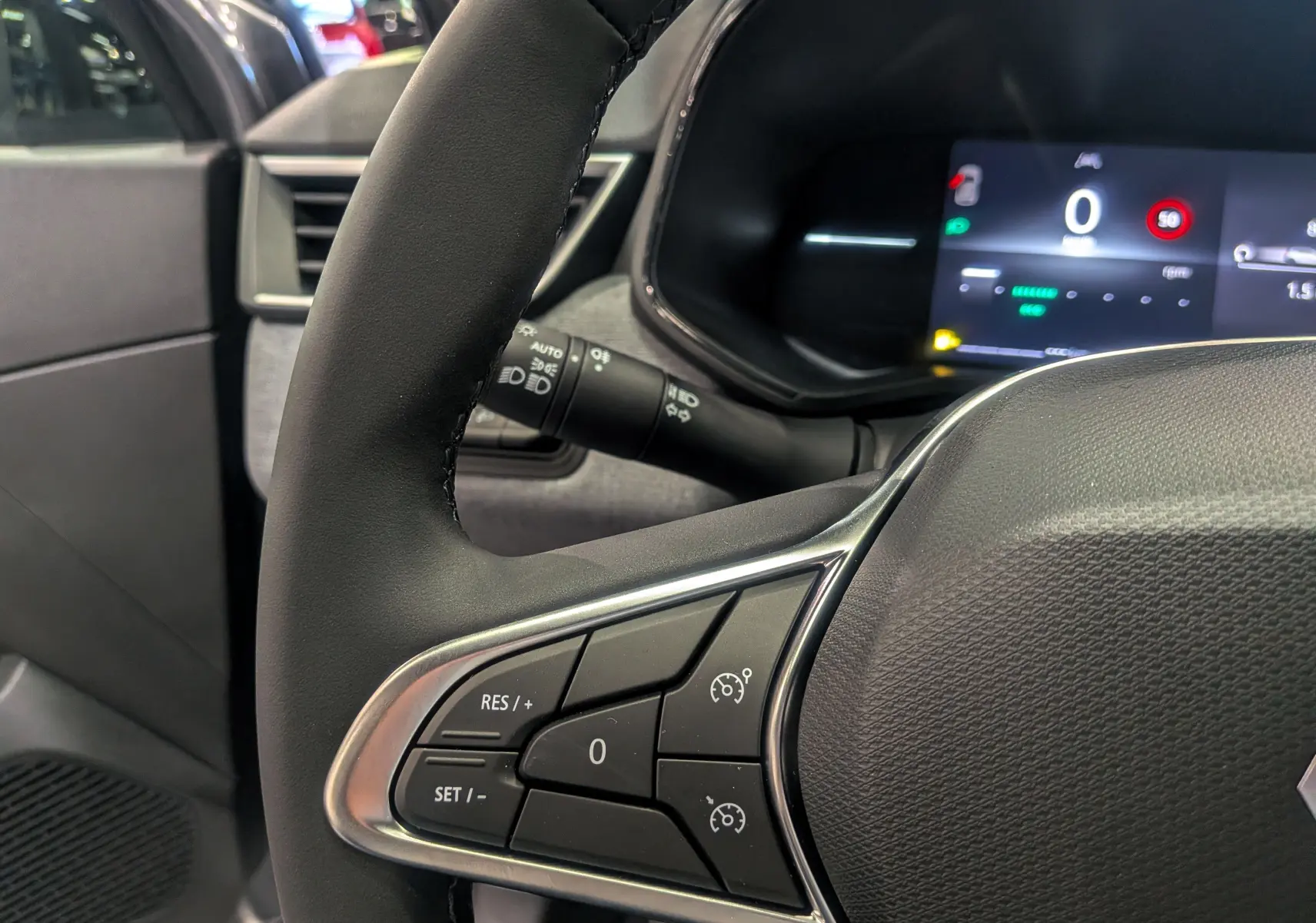 Gros plan sur le volant côté gauche de la Renault Clio V gris schiste, avec commandes de régulateur et tableau de bord numérique.