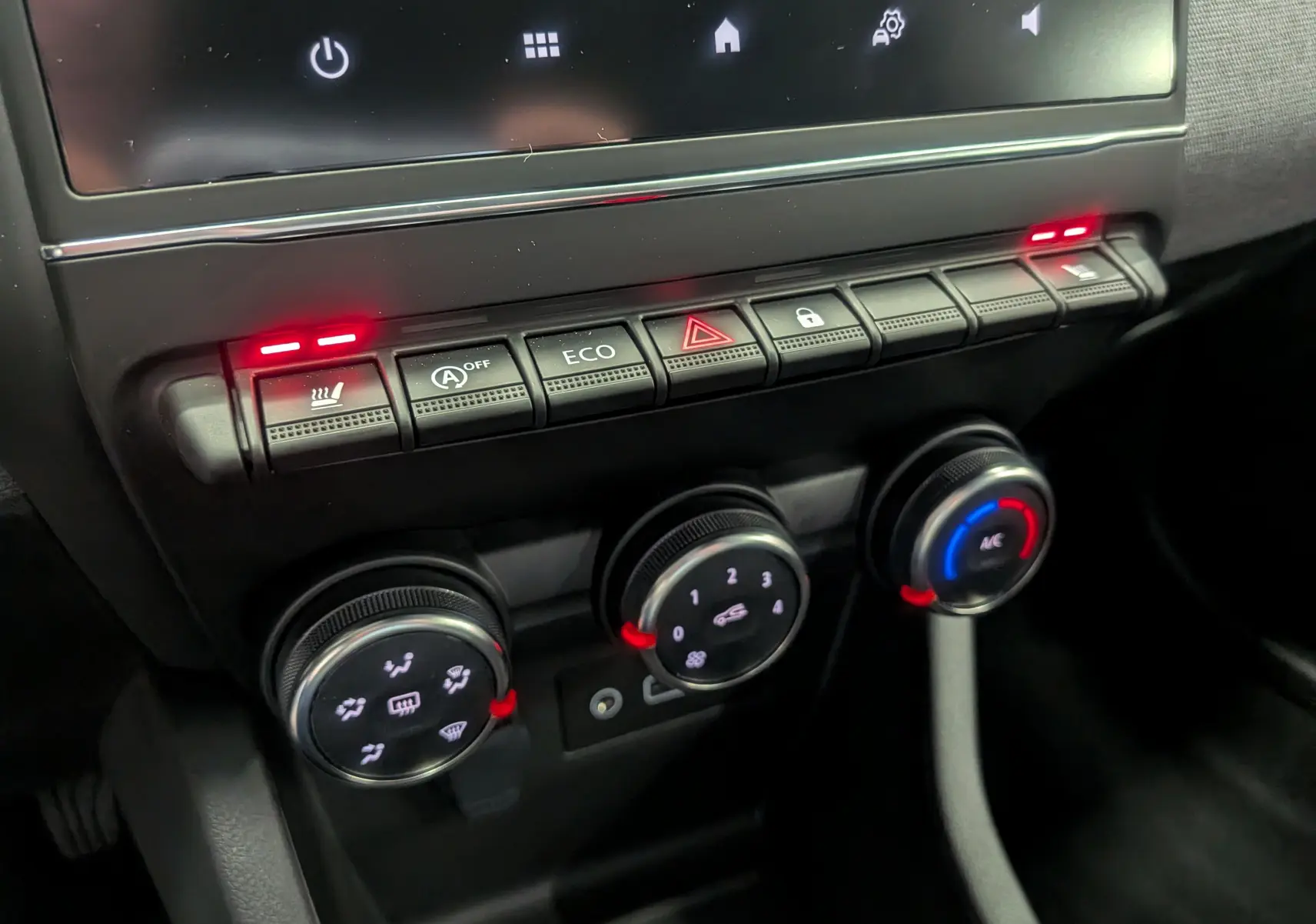 Vue rapprochée de la console centrale de la Renault Clio V gris schiste, avec commandes climatisation et boutons éclairés.