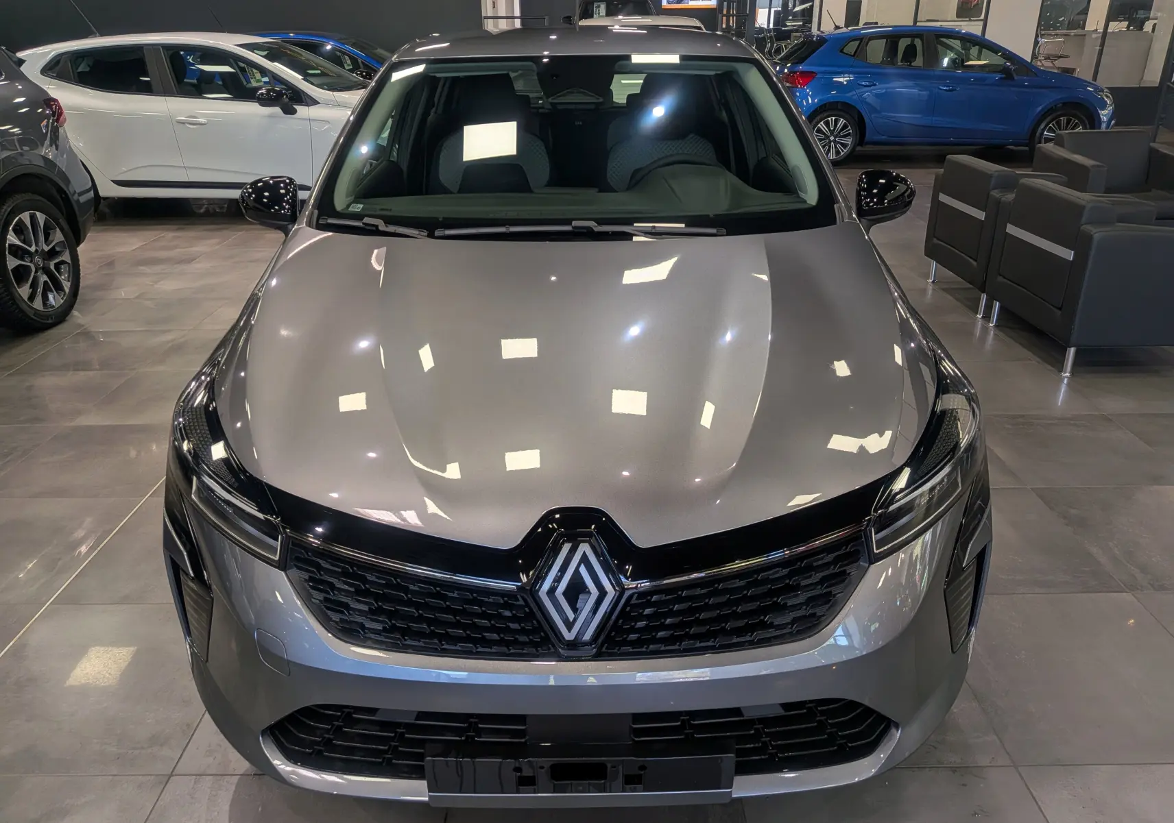 Vue avant d'une Renault Clio V gris schiste dans un showroom, mettant en valeur sa calandre noire et ses phares fins.