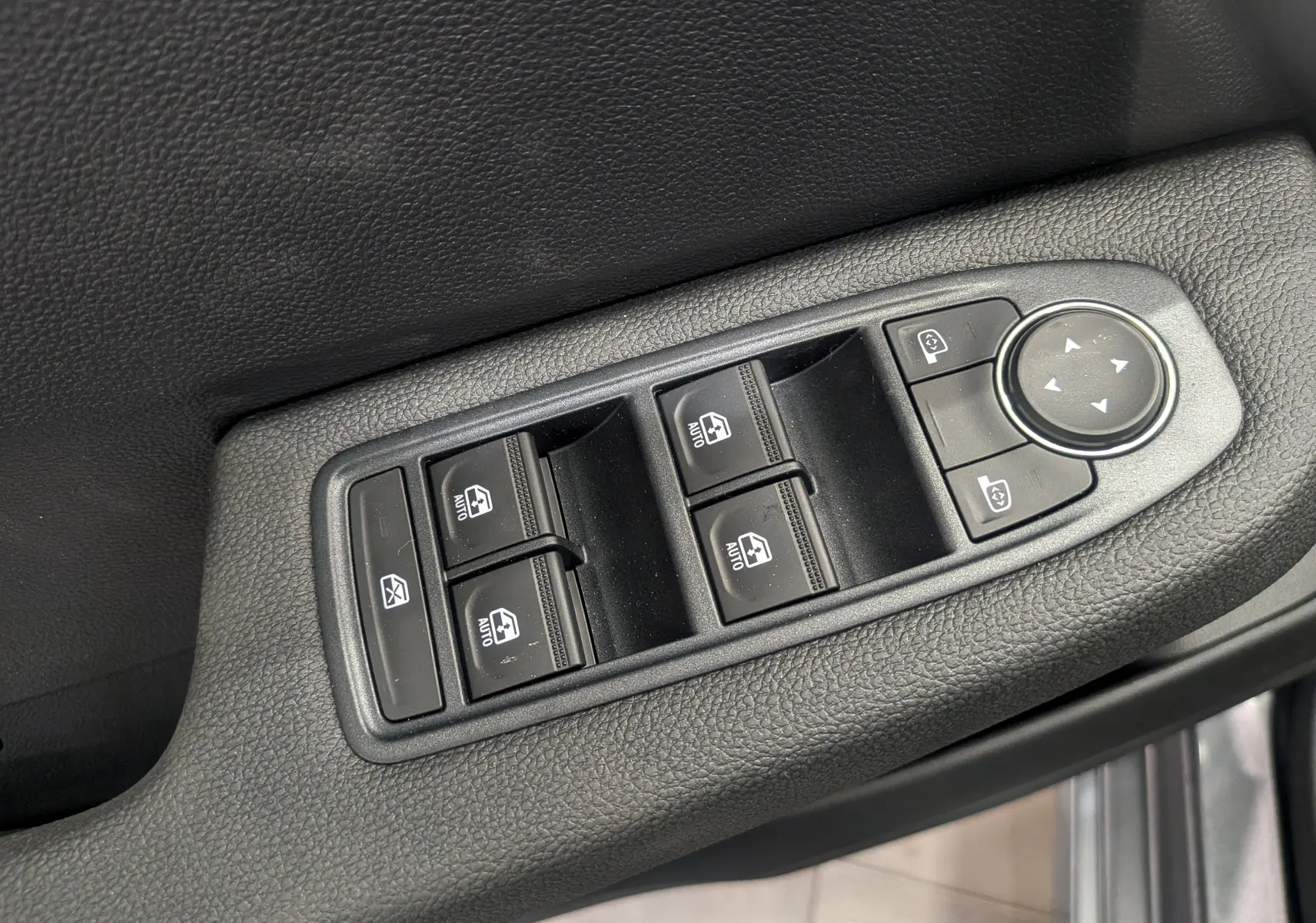 Gros plan sur les commandes de lève-vitres et réglage des rétroviseurs côté conducteur, finition tissu noir.