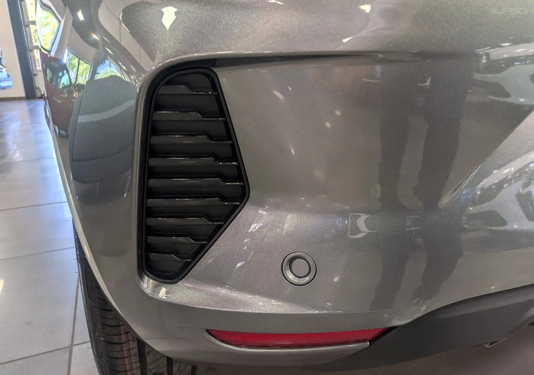 Gros plan sur l'angle arrière gauche de la Renault Clio V gris schiste, montrant la grille d'aération et le capteur de recul.
