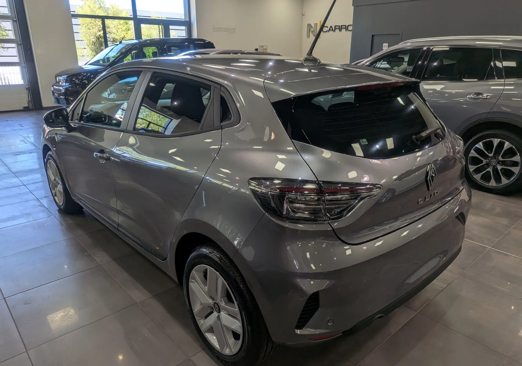 Renault Clio V Blue dCi 100 gris schiste vue 3/4 arrière droit en intérieur, avec feux arrière LED et antenne toit.