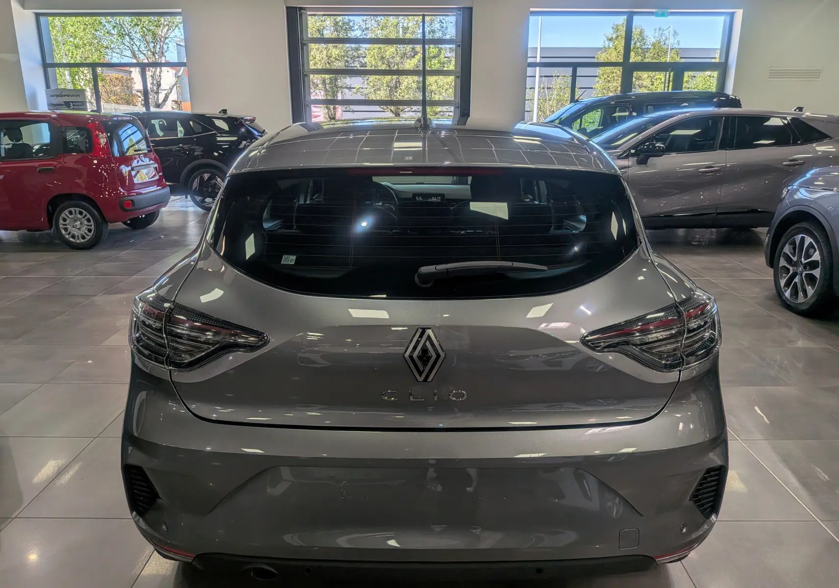 Vue arrière d'une Renault Clio V gris schiste dans un showroom, mettant en valeur ses feux arrière et son logo central.